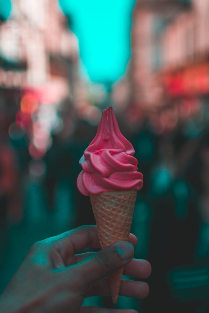 A hand-held pink ice cream cone on a bustling Paris street.