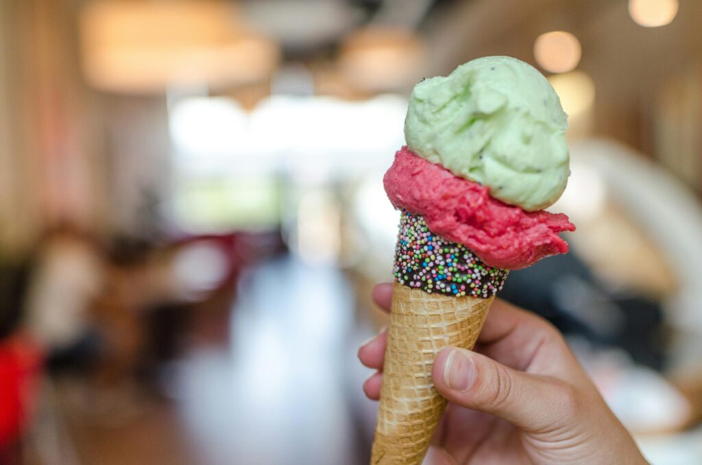 Hand holding a vibrant ice cream cone with sprinkles indoors, perfect summer treat.